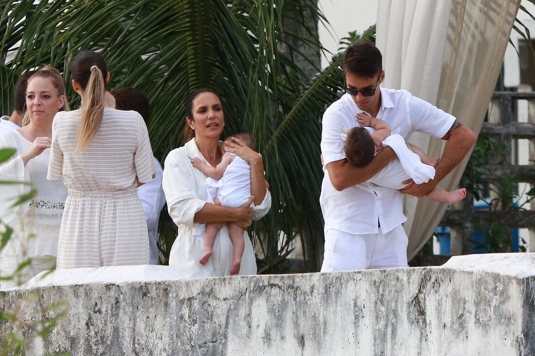Ivete Sangalo e Daniel Cady seguram as gêmeas no colo para ir a pia batismal