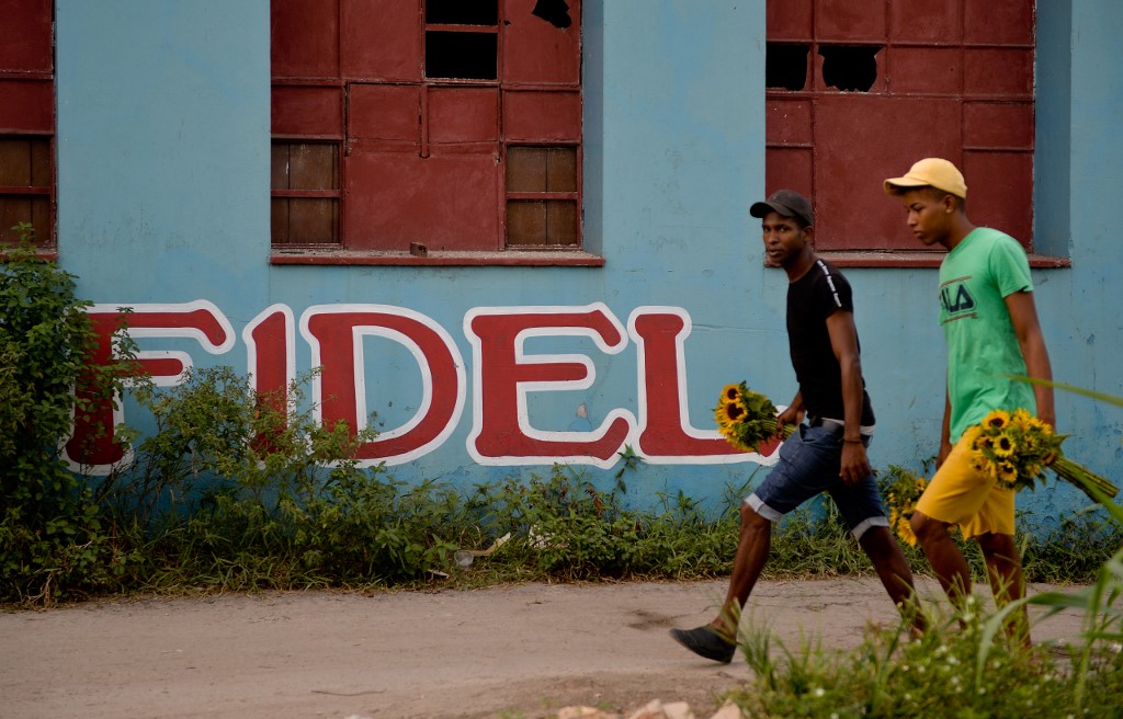 Cubanos andam ao lado da parede lendo Fidel em uma rua de Havana