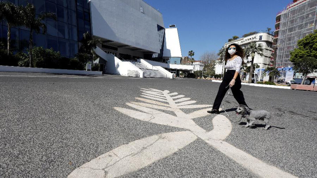 Mulher usando máscara de proteção passeia com cachorro sobre símbolo da Palma de Ouro em frente ao Palácio do Festival em Cannes