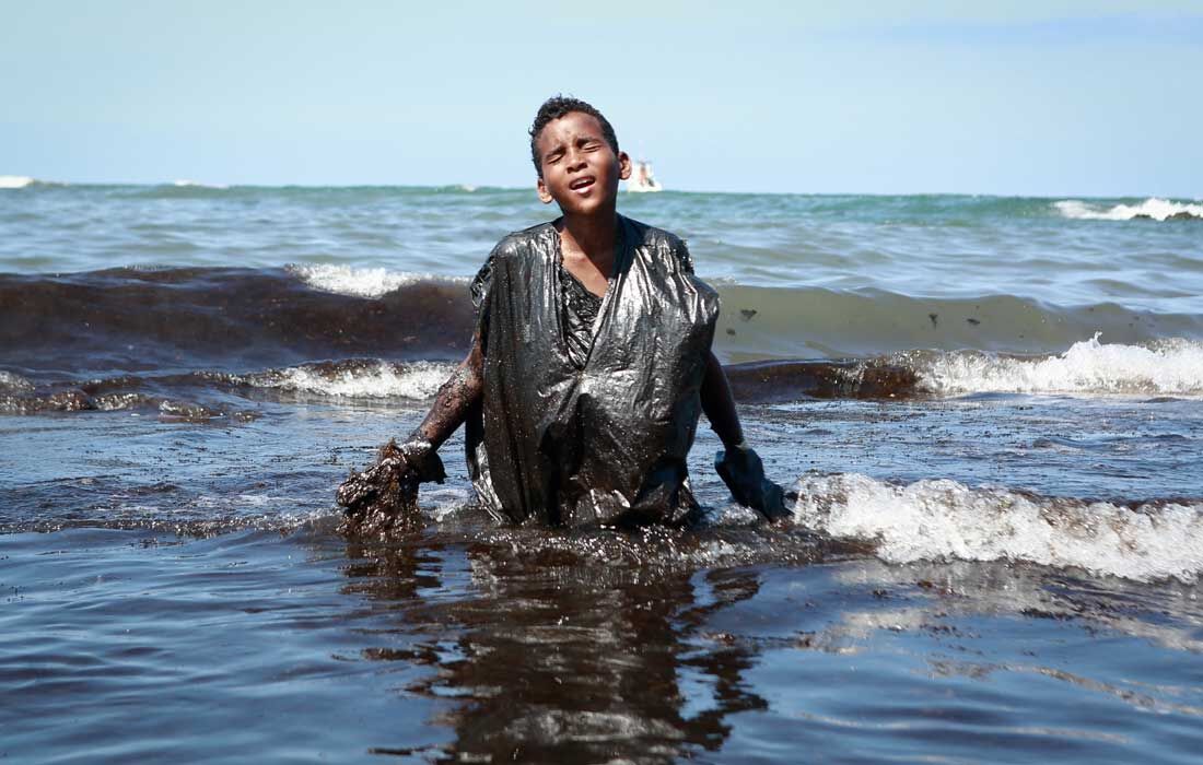 Menino ajudando na limpeza de mancha de óleo em praia de Pernambuco, em 2019