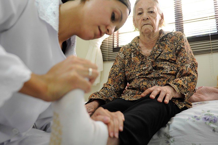 Fisioterapeuta atende idosa em casa, em Brasília 