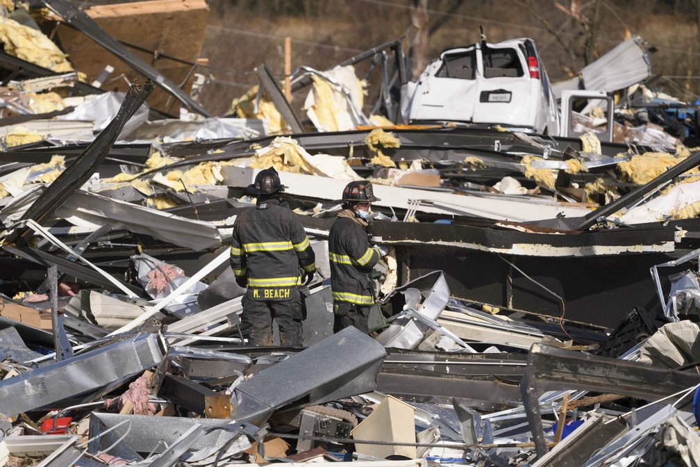 Em Mayfield, integrantes de equipe de emergência vasculham escombros da fábrica de velas em Mayfield, na qual mais de cem pessoas trabalhavam quando o tornado passou. Dezenas morreram e muitos ainda estão desaparecidos