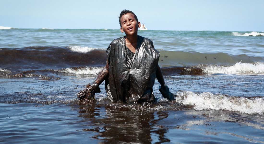 Garoto sujo de óleo na praia de Itapuama, no litoral pernambucano, em outubro de 2019