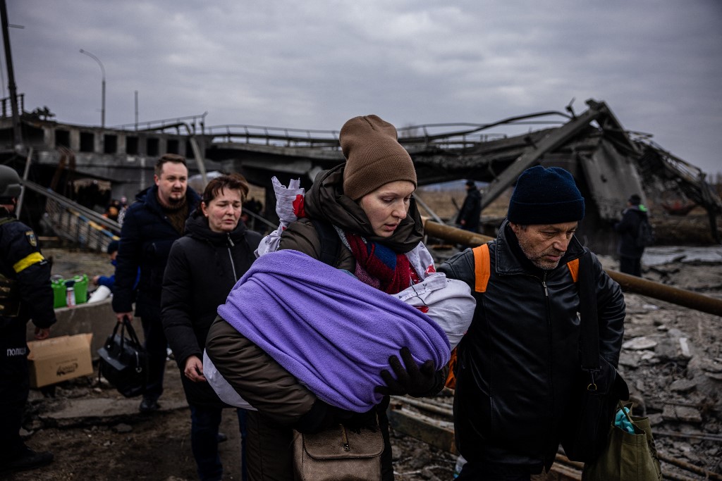 Uma mulher carregando seu bebê atravessa uma ponte destruída ao fugir da cidade de Irpin, a noroeste de Kiev, em 7 de março de 2022