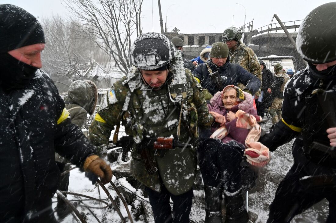 Soldados ucranianos ajudam uma idosa a atravessar uma ponte destruída enquanto ela evacua a cidade de Irpin, a noroeste de Kiev, em 8 de março de 2022.