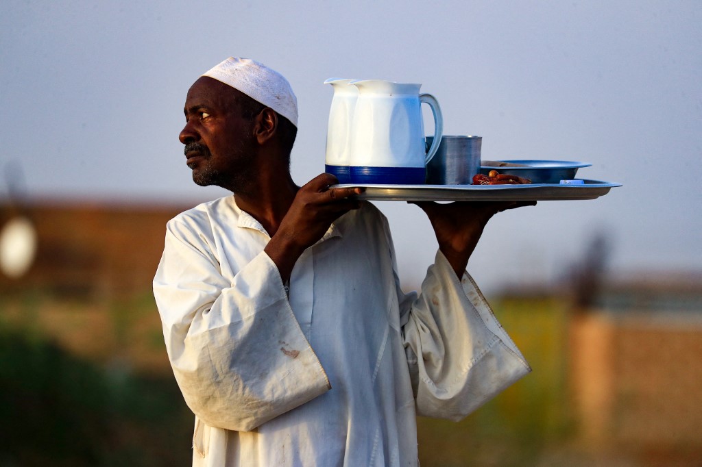 Um homem serve comida e bebidas uma refeição coletiva Iftar em frente a uma mesquita ao longo da rodovia estadual Jazeera na vila de al-Nuba, cerca de 50 quilômetros ao sul da capital do Sudão, em 8 de abril de 2022, durante o mês sagrado muçulmano do Ram