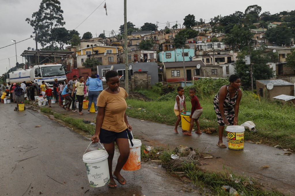 Moradores do assentamento de Bhambayi caminham com baldes cheios de água após enchê-los de um caminhão-tanque como resultado de interrupções por fortes chuvas e inundações na rodovia M25 em Inanda, norte de Durban, em 13 de abril de 2022