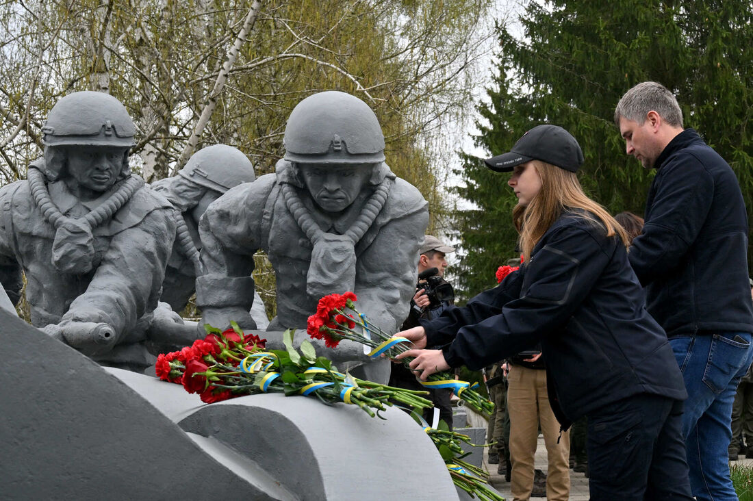 Pessoas colocam flores no monumento em Chernobyl para homenagear os bombeiros que morreram durante o desastre de Chernobyl em 1986 na Usina Nuclear de Chernobyl, em 26 de abril de 2022.