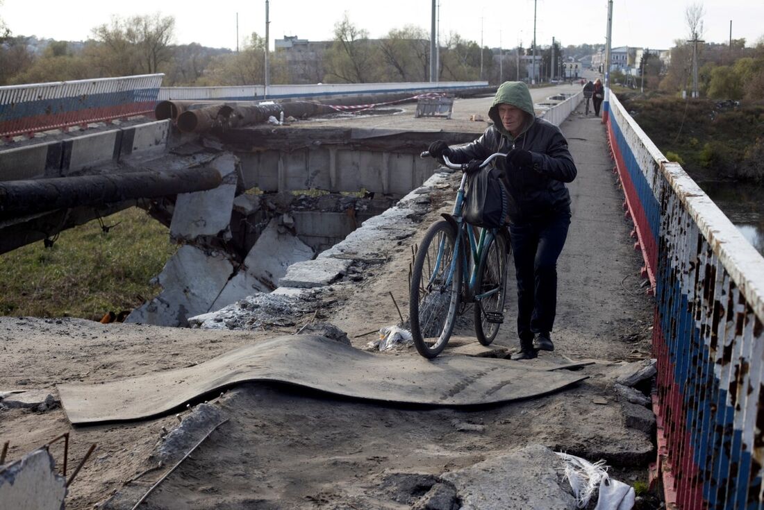 Um morador local empurra sua bicicleta em uma ponte destruída perto de Borivske, região de Kharkiv, em 23 de outubro de 2022