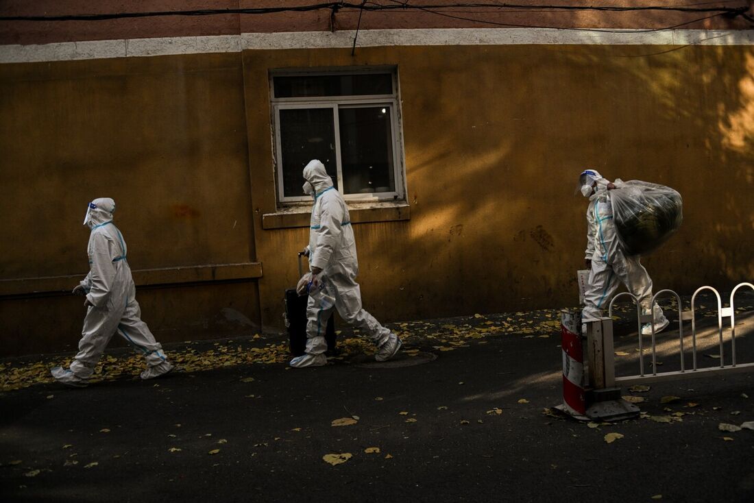 Pessoas usando equipamento de proteção individual (EPI) caminham perto de uma área residencial sob bloqueio devido às restrições do coronavírus Covid-19 em Pequim em 26 de novembro de 2022