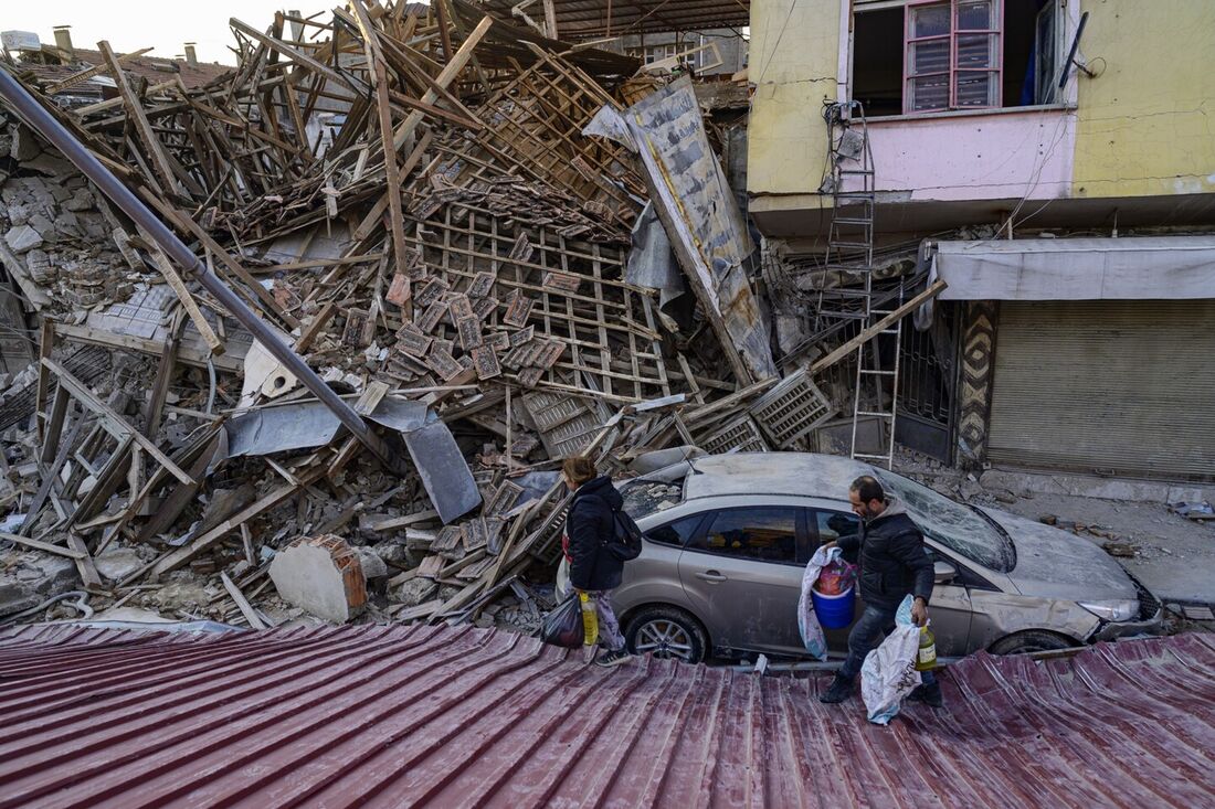 Um homem e uma mulher caminham sobre os escombros de um prédio destruído após dois terremotos consecutivos que afetaram a Turquia e a Síria no início da semana, em Antakiya, província de Hatay, sul da Turquia, em 10 de fevereiro de 2023