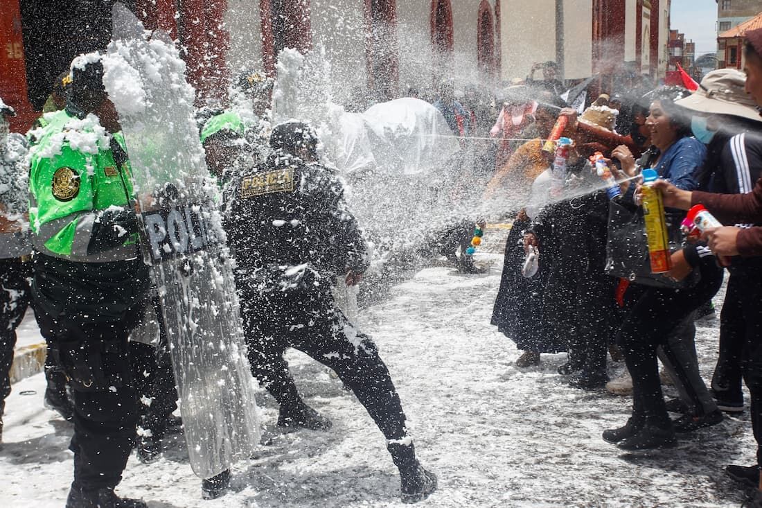 Pessoas marchando em homenagem aos que morreram durante confrontos com a polícia nas manifestações contra a presidente peruana Dina Boluarte, param a manifestação e brincam com a polícia borrifando água e espuma como tradição do carnaval em Puno, Peru