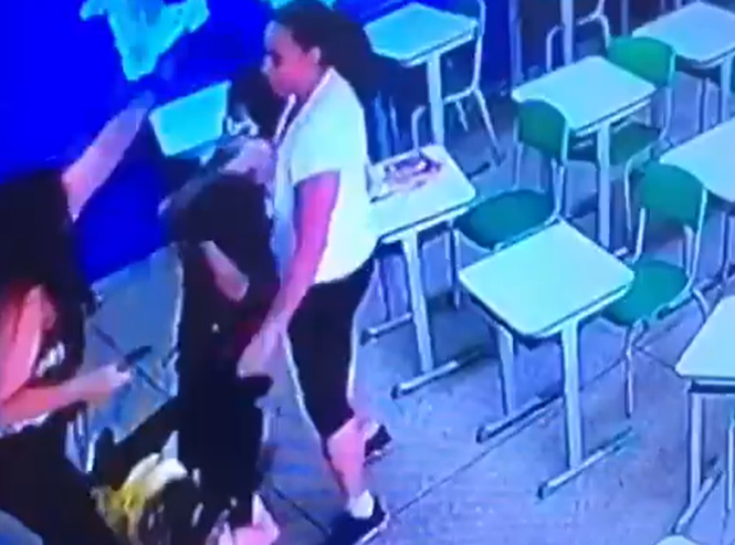 A mulher segura a mão do garoto e dá um "mata-leão" nele, até que uma outra funcionária da escola surge e toma o objeto do agressor