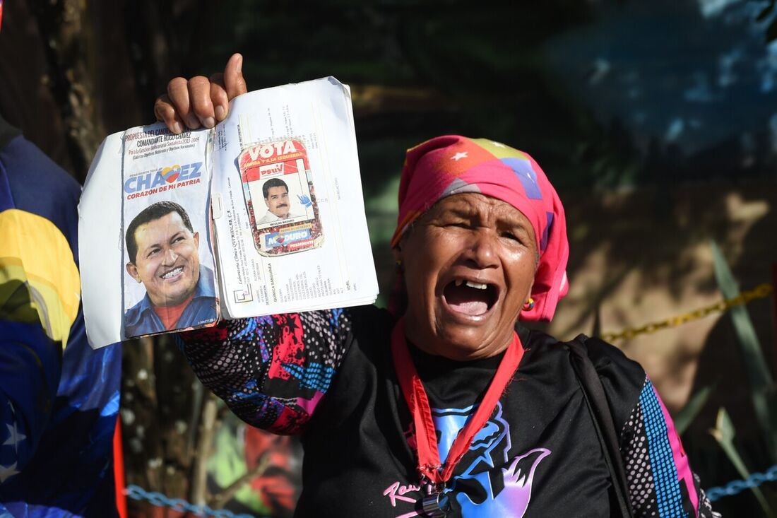 Mulher segura caderno com fotos de Chávez e Maduro