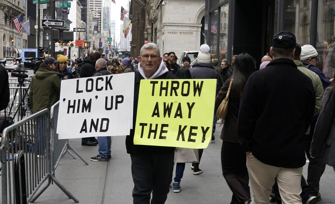 Um manifestante carrega cartazes contendo os seguintes dizeres: "tranquem ele e joguem a chave fora", em frente à Trump Tower em Nova York em 31 de março de 2023, na manhã seguinte ao ex-presidente Donald Trump ser indiciado