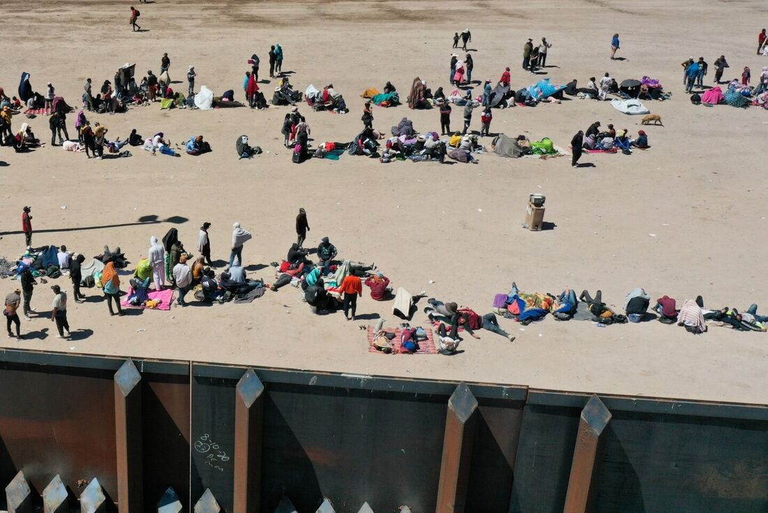 Migrantes esperando ao longo do muro da fronteira para se renderem aos agentes da patrulha de fronteira da Alfândega e Proteção de Fronteiras (CBP) dos EUA para processamento de pedidos de asilo e imigração após cruzarem o Rio Grande para os EUA.