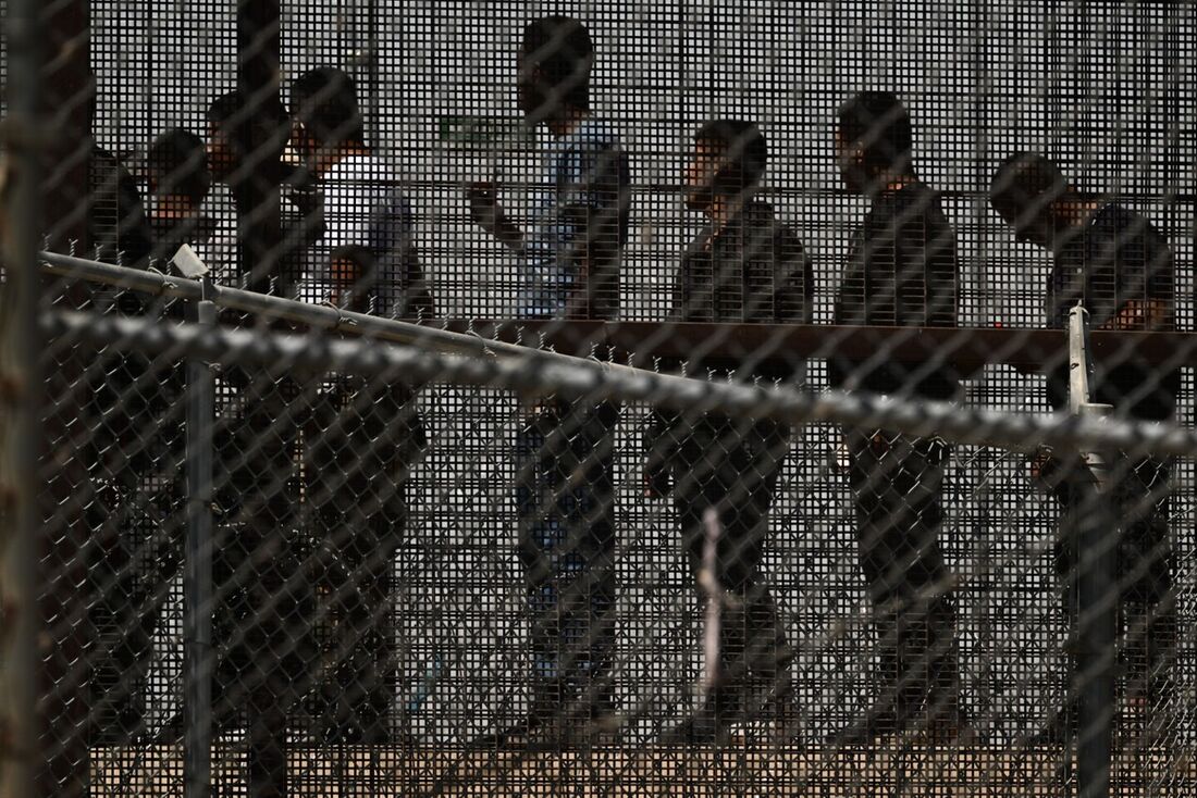 Migrantes esperam ao longo do muro da fronteira para embarcar em um ônibus depois de se entregarem aos agentes da Patrulha de Fronteira da Alfândega e Proteção de Fronteiras (CBP) dos EUA para processamento de pedidos de imigração e asilo.