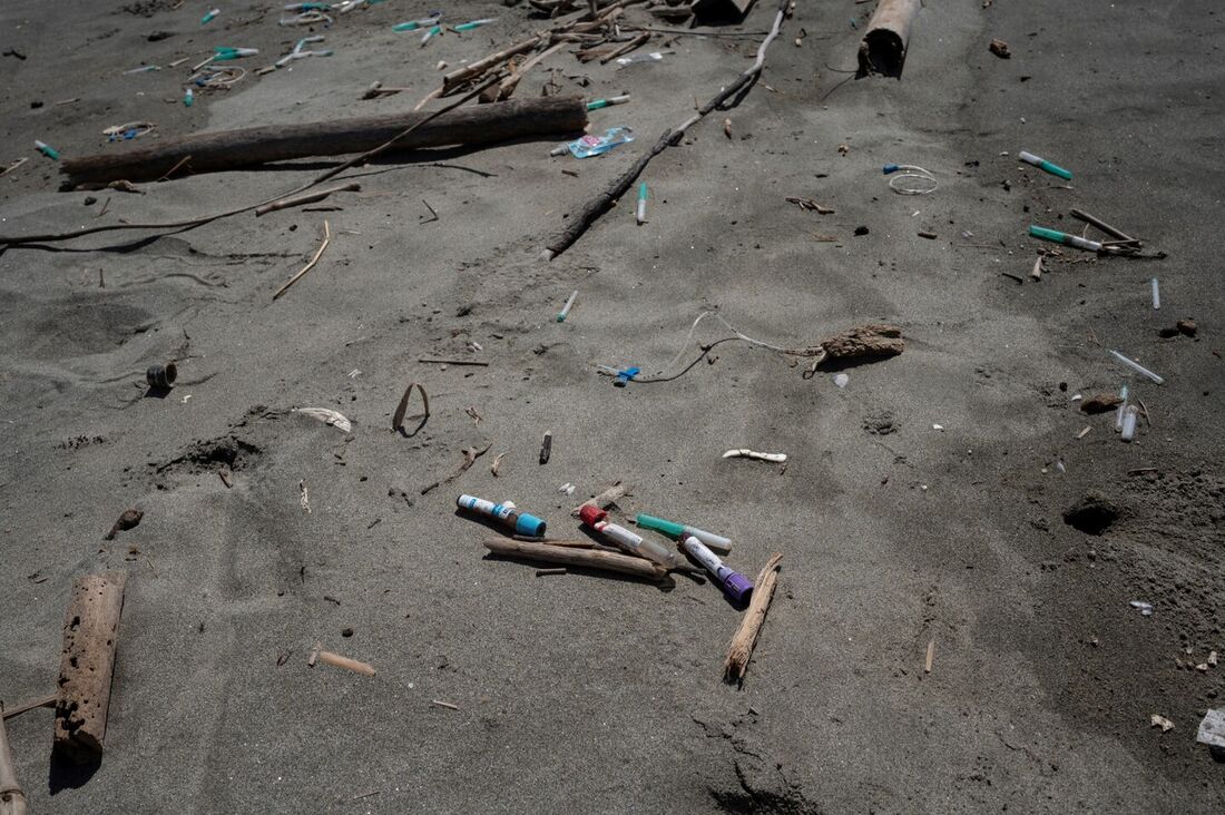 Cateteres e tubos de ensaio com resíduos de amostras de sangue de laboratório são vistos ao lado de uma toca de caranguejo na praia de Paparo, no estado de Miranda, Venezuela, em 6 de junho de 2023