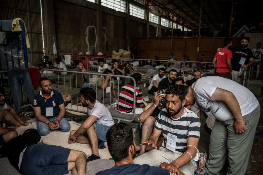 Sobreviventes de um naufrágio sentam-se dentro de um armazém no porto da cidade de Kalamata, em 15 de junho de 2023, depois que um barco transportando migrantes afundou em águas internacionais no Mar Jônico