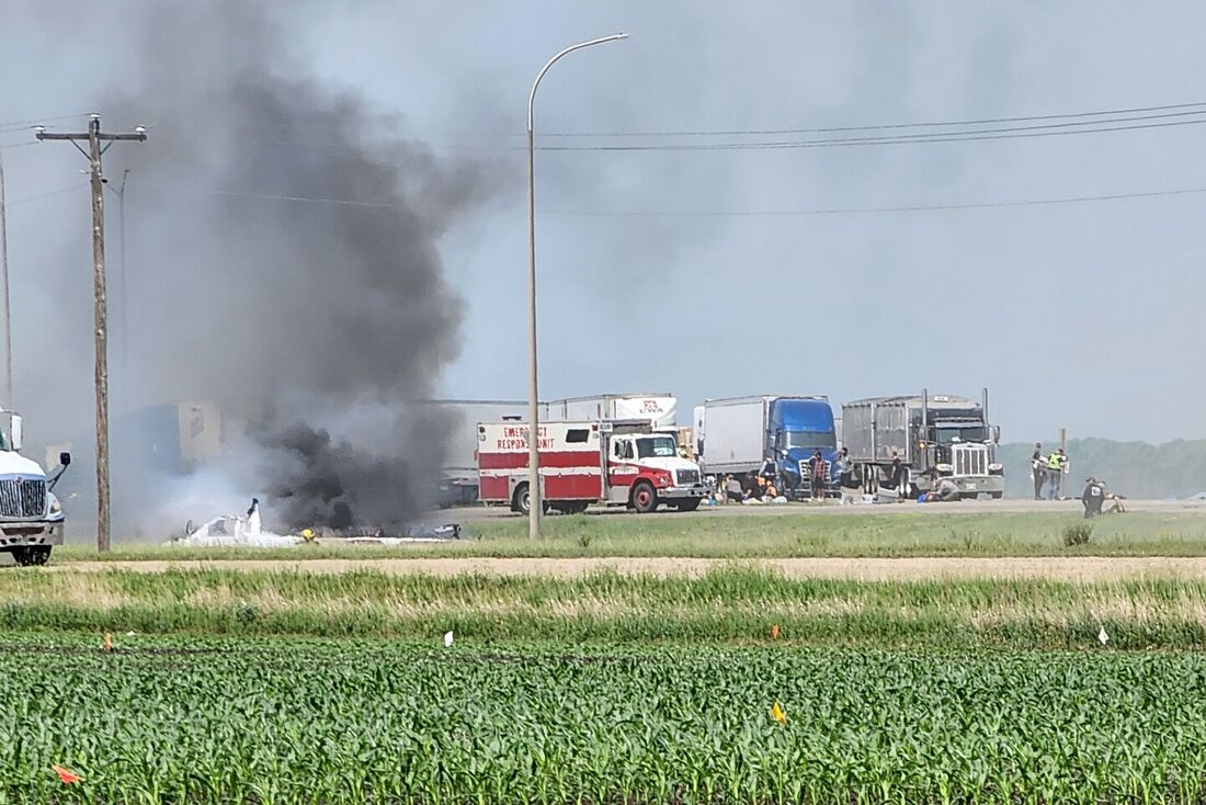 Fumaça sai de um carro enquanto socorristas são fotografados após um acidente de viação que deixou 15 mortos perto de Carberry, a oeste de Winnipeg, Canadá, em 15 de junho de 2023