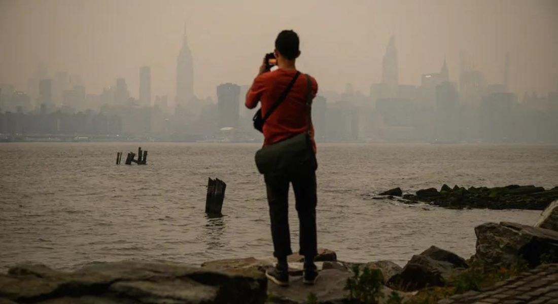 Homem observa a cidade de Nova York coberta por uma névoa cinza após incêndios no Canadá