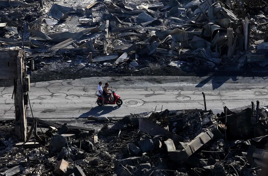 Em uma vista aérea, dois homens andam de scooter por empresas que foram destruídas pelo incêndio florestal de 11 de agosto de 2023 em Lahaina, Havaí