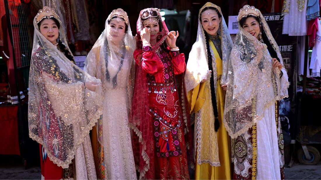 Mulheres vestindo trajes tradicionais uigures posando para uma foto na área turística de Old Kashgar, na região de Xinjiang, no noroeste da China