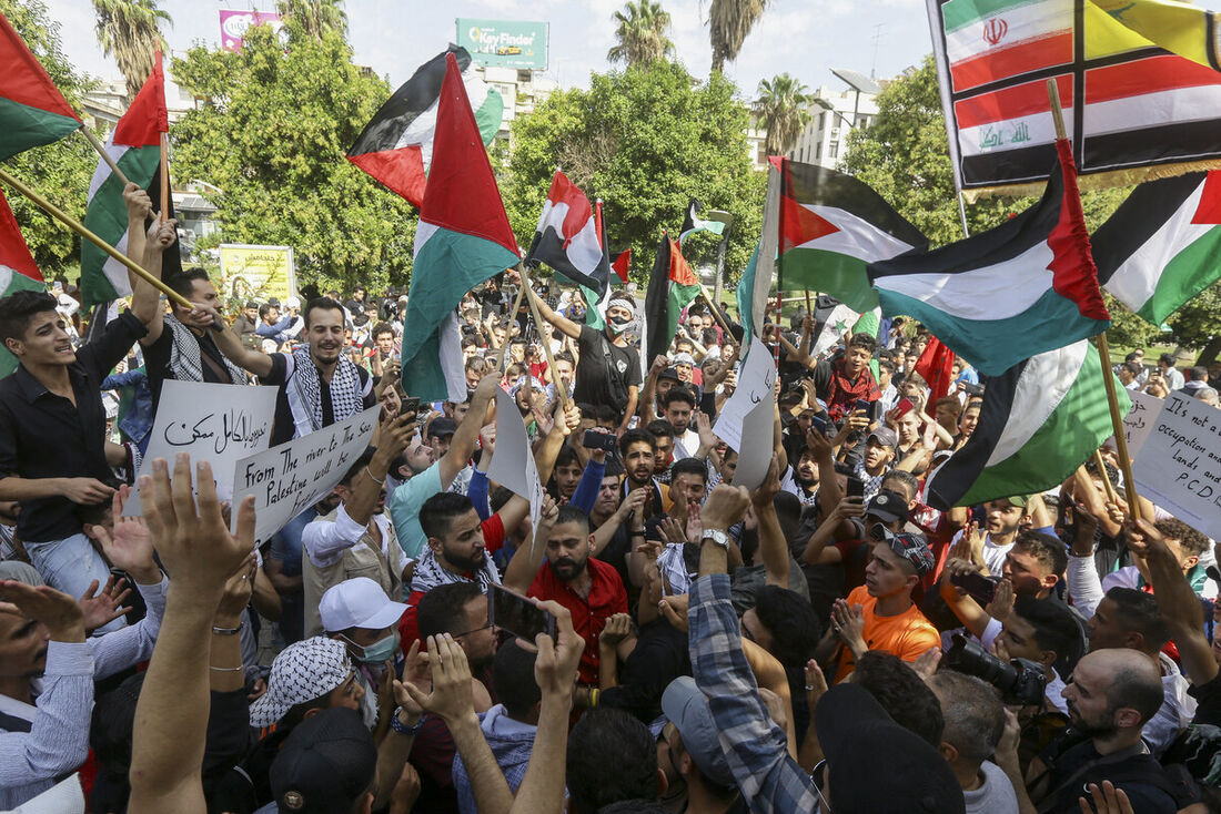 Pessoas agitam bandeiras nacionais sírias e palestinas durante uma manifestação em solidariedade ao povo da Palestina 