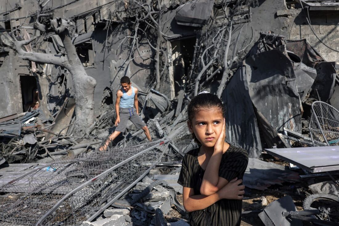 Menina observa enquanto fica perto dos escombros do lado de fora de um prédio que foi atingido pelo bombardeio israelense em Rafah, no sul da Faixa de Gaza