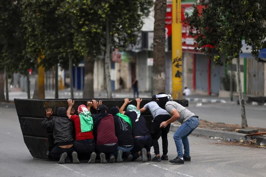 Jovens palestinos se escondem atrás de barricada durante manifestação de apoio a Gaza na Cisjordânia ocupada 