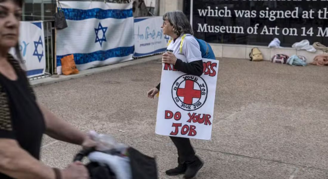 Mulher carrega cartaz que diz 'Cruz Vermelha Faça o Seu Trabalho' durante manifestação pela libertação de reféns, em Tel Aviv 