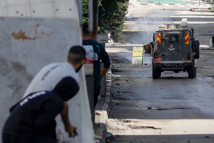 Palestinos se escondem atrás de muro após confronto entre manifestantes e forças de segurança de Israel no campo de refugiados de Balata, na Cisjordânia 