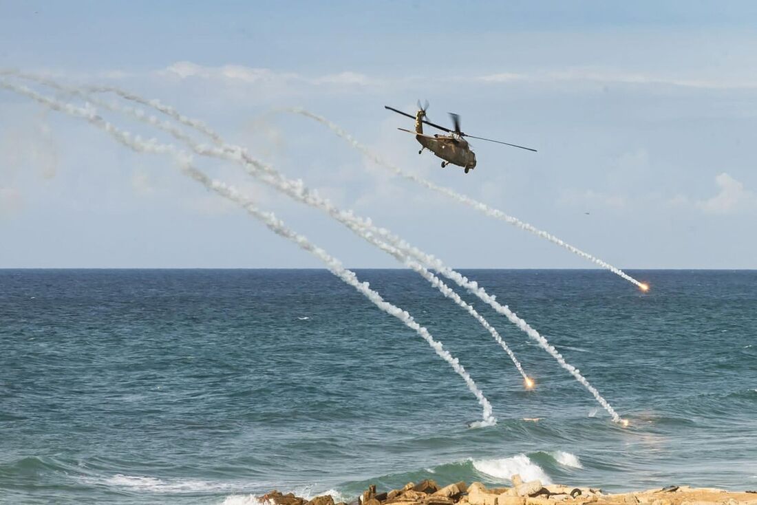 Helicóptero israelense disparando sinalizadores enquanto sobrevoa uma praia na Faixa de Gaza, em meio a batalhas entre Israel e o grupo palestino Hamas