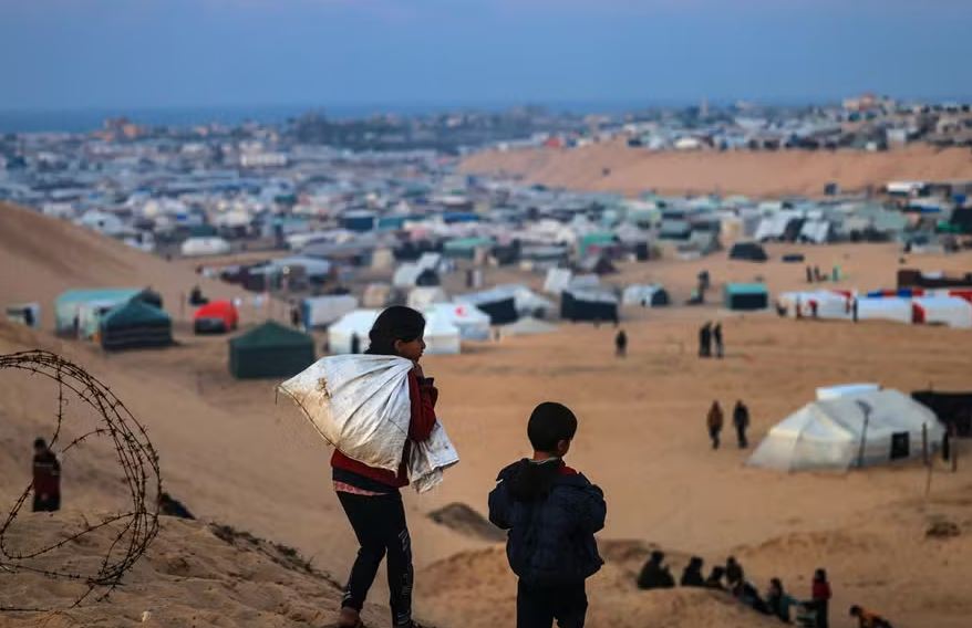 Crianças palestinas deslocadas caminham em uma colina em frente ao seu acampamento improvisado em Rafah, no sul da Faixa de Gaza, na fronteira com o Egito 