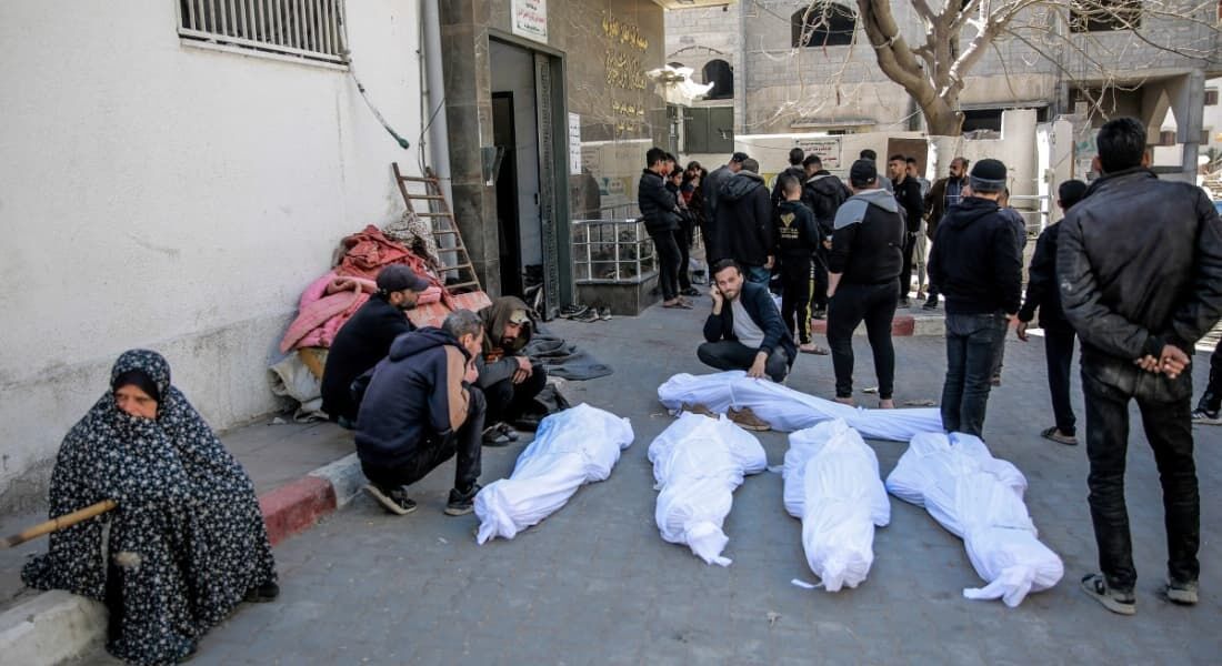 Palestinos ao lado de corpos de conterrâneos mortos ao correrem em direção a caminhões de ajuda humanitária na Cidade de Gaza