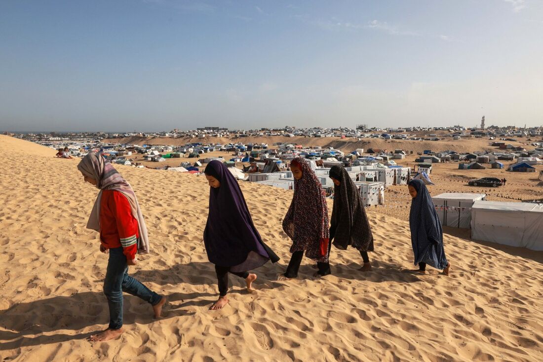 Meninas palestinas caminham em uma duna de areia em um campo para deslocados em Rafah, no sul da Faixa de Gaza