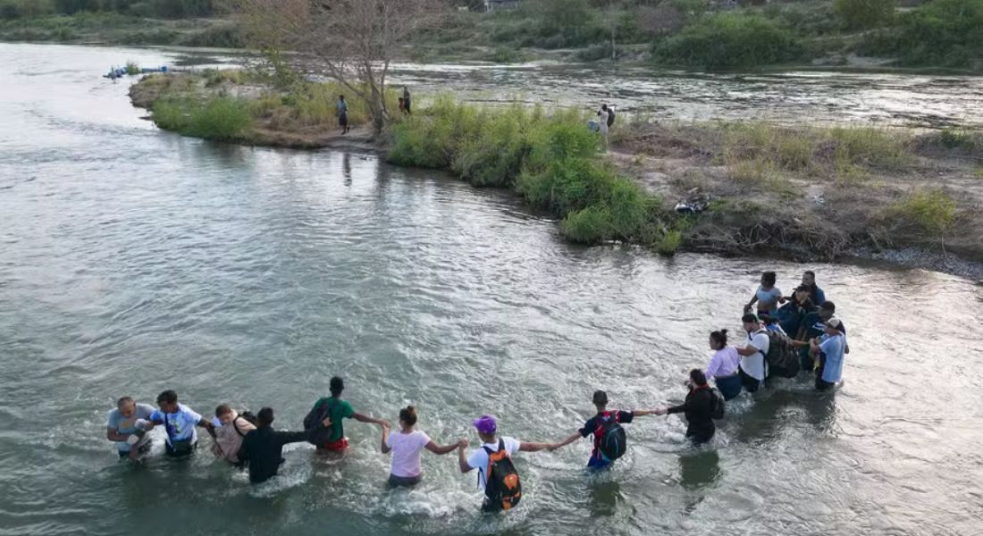 Grupo de migrantes de mãos dadas enquanto cruzam o Rio Grande, na fronteira entre os EUA e o México, para Eagle Pass, Texas