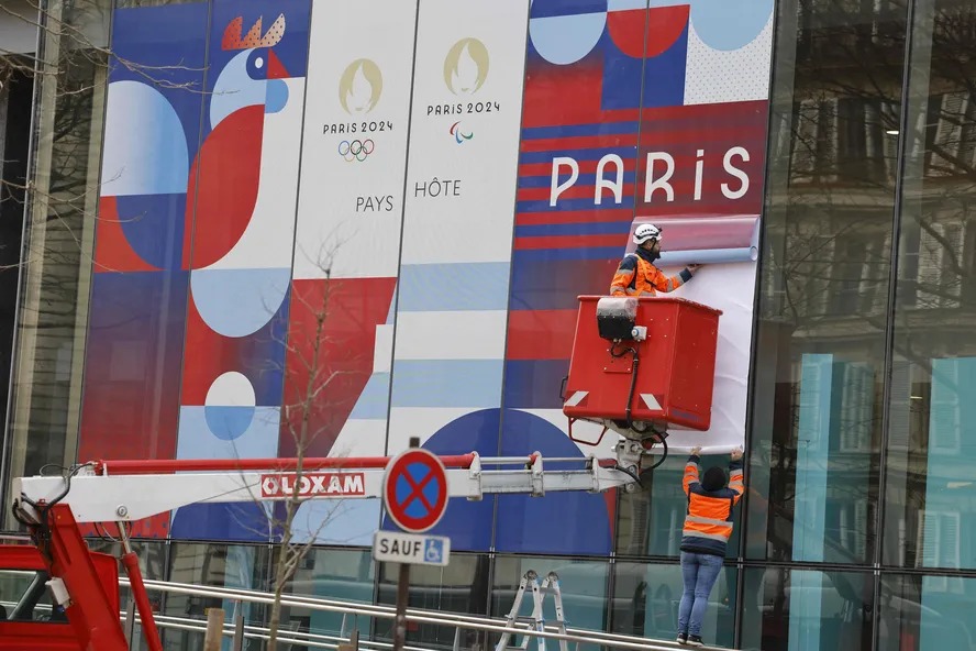 Trabalhadores montaram um cartaz gigante anunciando os Jogos Olímpicos na fachada do Ministério da Solidariedade e Saúde em Paris 