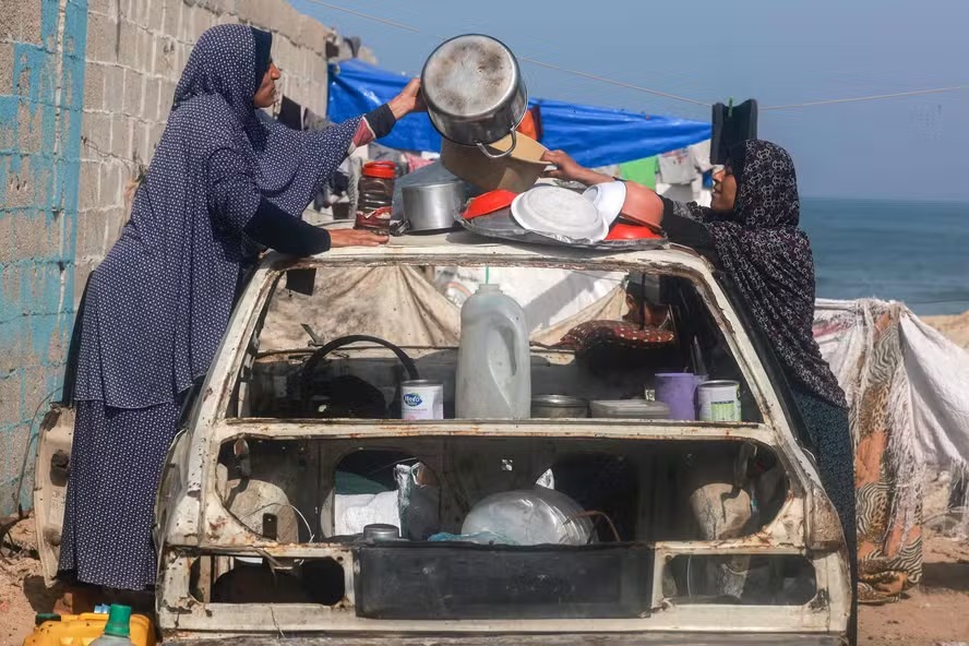 Palestinas organizam utensílios de cozinha em cima de carro destruído em Rafah