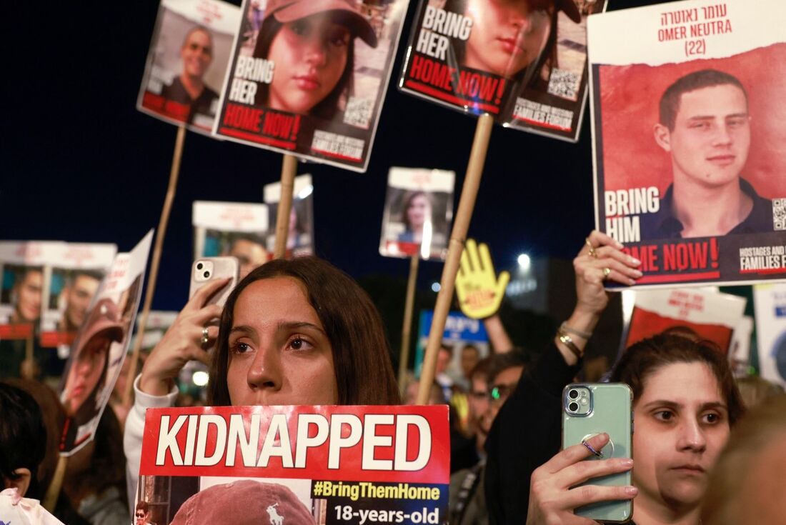 Parentes e apoiadores de reféns israelenses detidos em Gaza seguram cartazes durante uma manifestação em frente ao parlamento israelense 