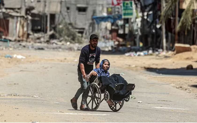 Um homem empurra uma mulher idosa em uma cadeira de rodas enquanto palestinos fogem de suas casas no campo de refugiados de Nuseirat, no centro da Faixa de Gaza. 