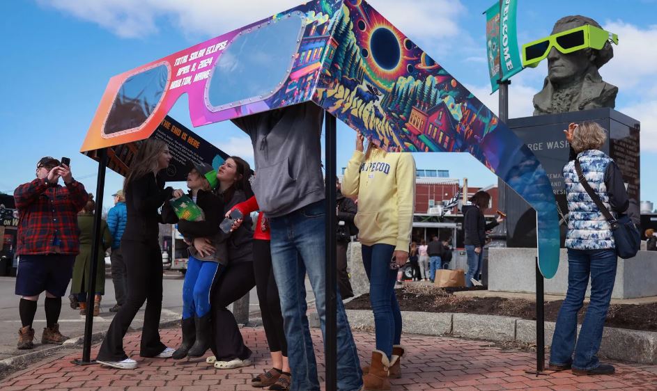 Visitantes olham através de um par de óculos gigante para eclipse montado na praça da cidade em Houlton, Maine. 