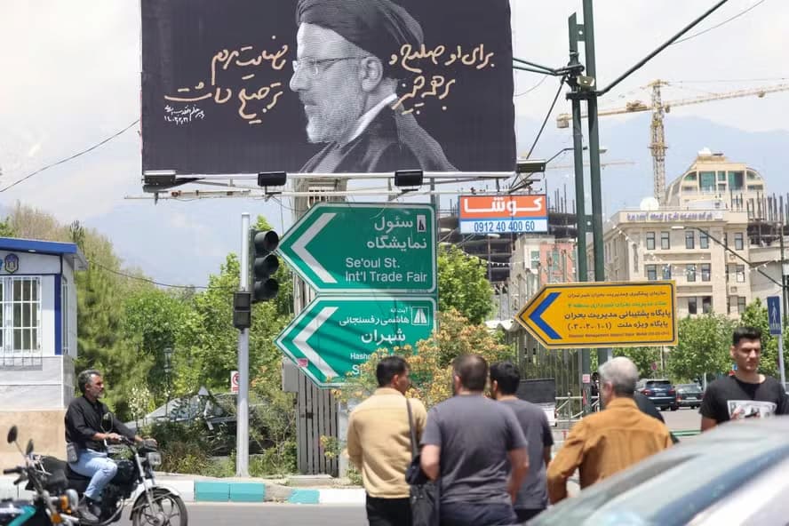 Pessoas atravessam uma estrada em frente a um outdoor com um retrato do falecido presidente do Irã, Ebrahim Raisi, no centro de Teerã, em 21 de maio de 2024.