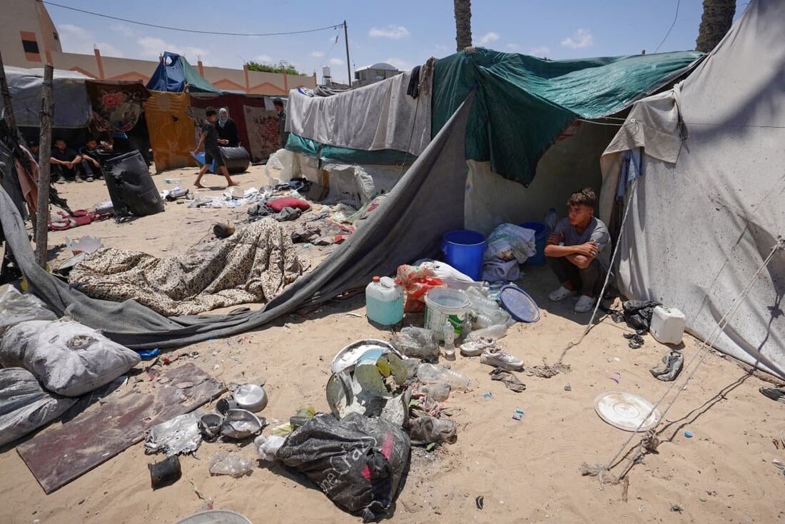 Palestinos deslocados sentam-se em suas tendas em um campo improvisado de deslocados na área de Mawasi, em Rafah, no sul da Faixa de Gaza