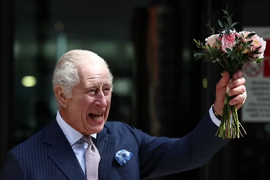 O rei Charles III acena e balança um buquê de flores durante sua visita ao Centro de Câncer Macmillan do Hospital Universitário de Londres