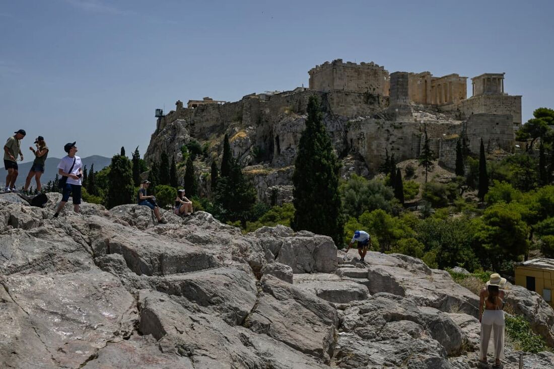 Pessoas ficam em frente à antiga colina da Acrópole durante um dia quente em Atenas