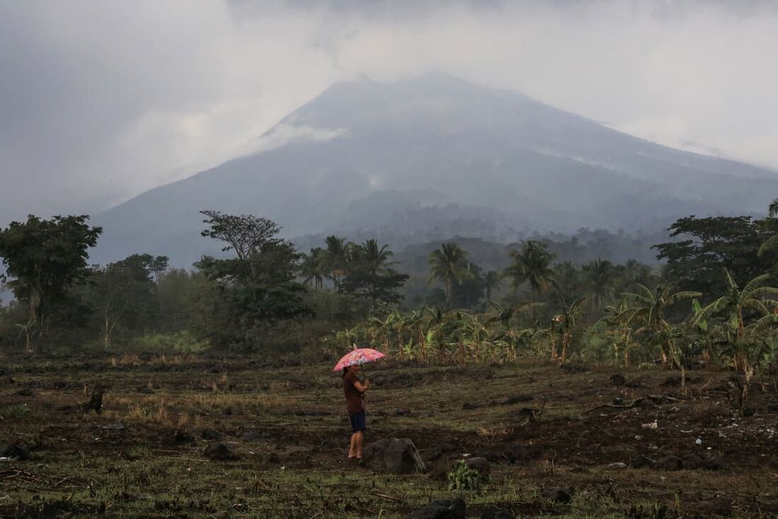 Um residente segurando um guarda-chuva fica perto de sua casa, no sopé do vulcão Monte Kanlaon, em um vilarejo em La Castellana, província de Negros Occidental, centro das Filipinas, em 4 de junho de 2024, um dia após a erupção do vulcão.