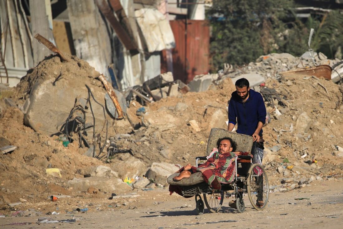 Um homem palestino empurra outro em uma cadeira de rodas passando pelos escombros do campo de refugiados de al-Maghazi, no centro da Faixa de Gaza