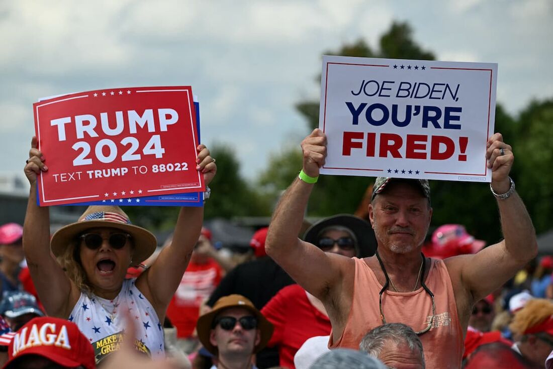 Apoiadores do ex-presidente dos EUA e candidato presidencial republicano Donald Trump seguram cartazes enquanto aguardam o comício de campanha de Trump