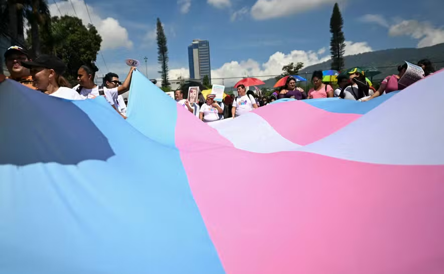 Membros de grupos LGBTQ+ seguram uma grande bandeira do Orgulho Trans durante comício que marca o Dia Internacional contra a homofobia, transfobia e bifobia em San Salvador, em 18 de maio de 2024. 